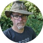 Martin Kalfatovic stands in front of vegetation, wearing a hat and glasses