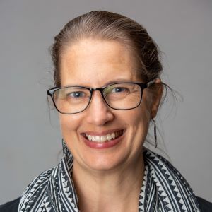 A woman with glasses, light brown hair, wearing a black and white scarf